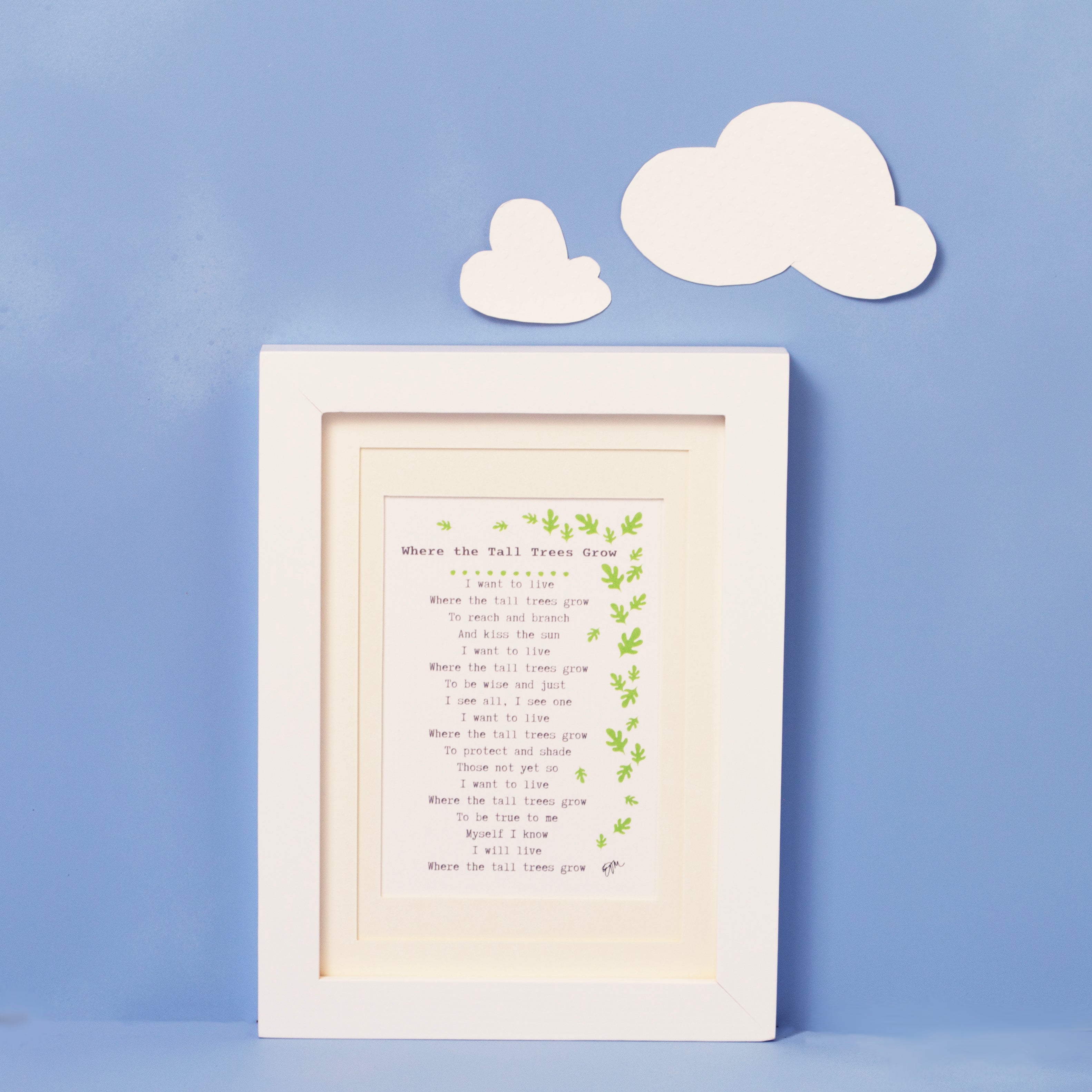 Baby's Poem is framed print of poem surrounded by a flurry of leaves.  The framed print is shot against a blue background with two white clouds above the framed print. The frame is white, and the matting is ivory