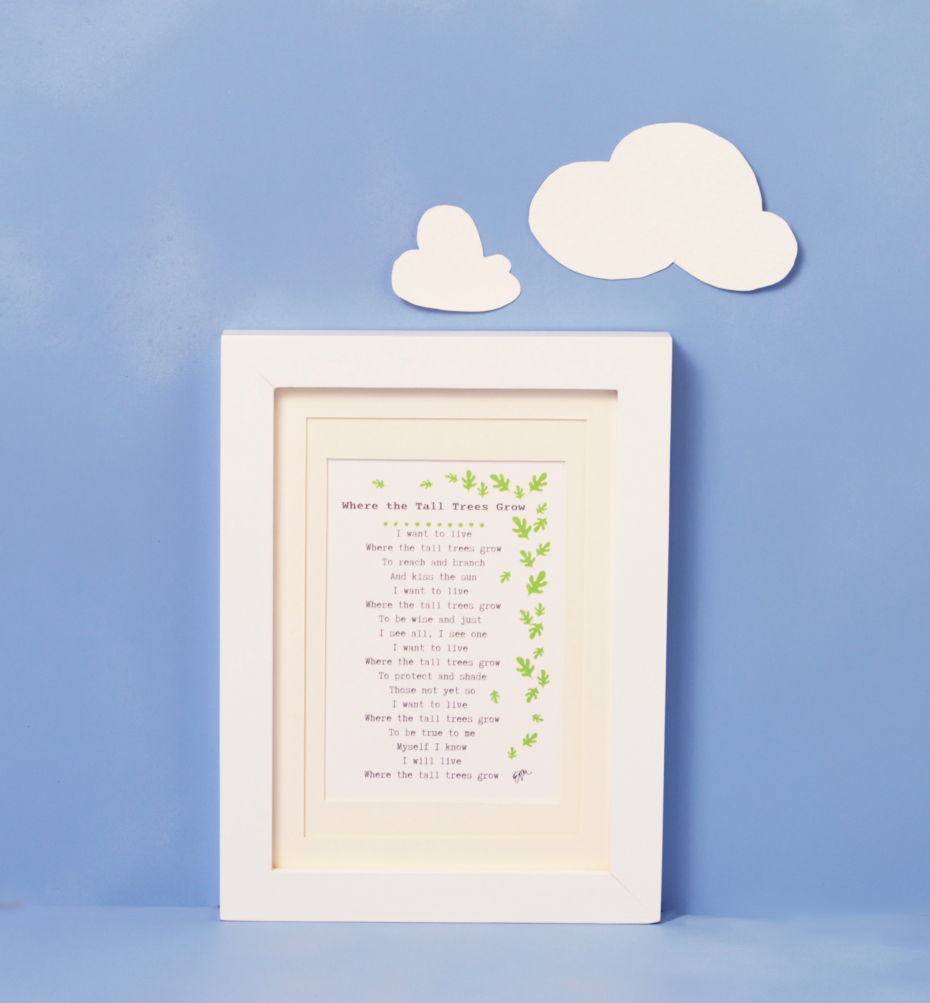Baby's Poem is framed print of poem surrounded by a flurry of leaves.  The framed print is shot against a blue background with two white clouds above the framed print. The frame is white, and the matting is ivory