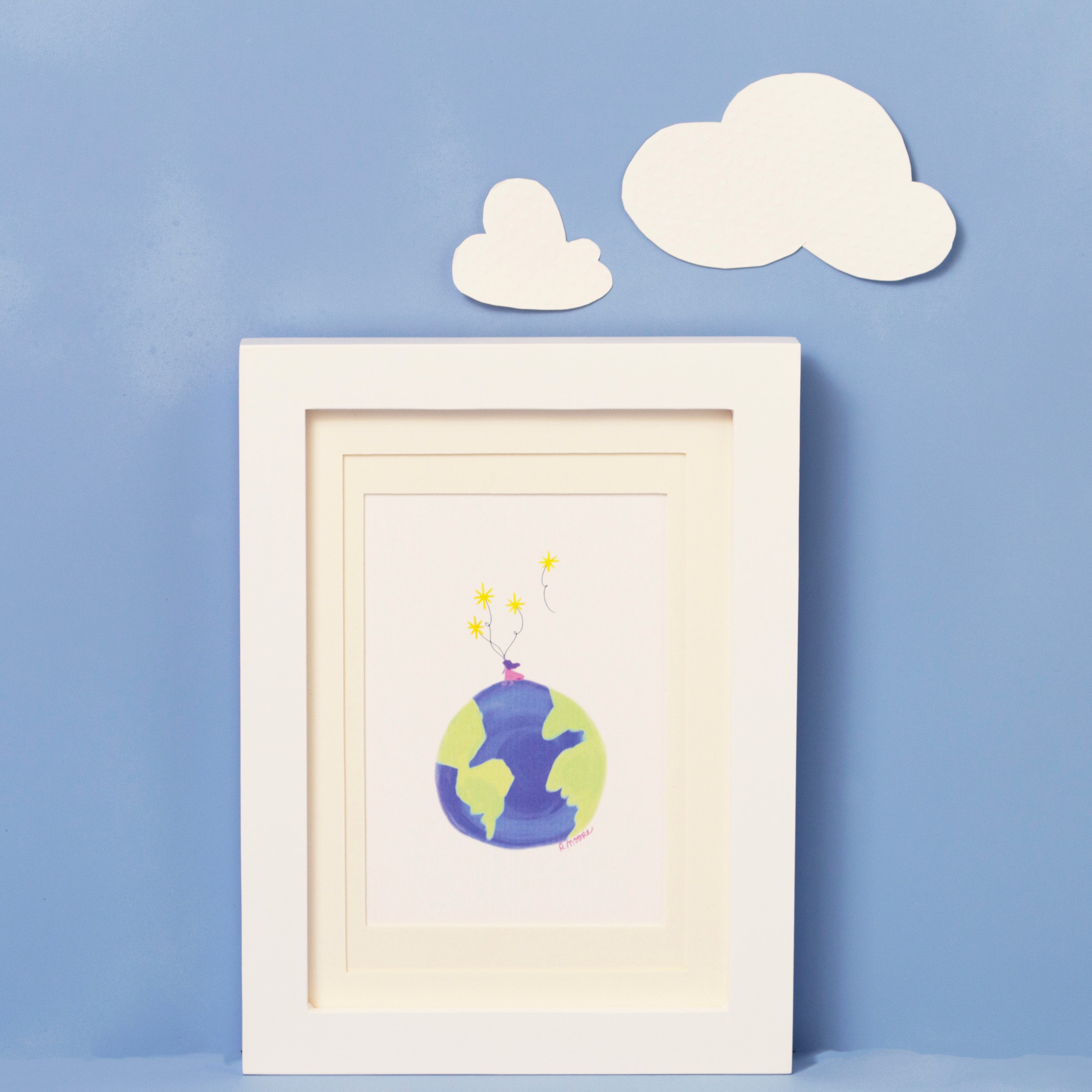 Girl on Top of the World framed print of a hand illustrated Girl in a pink dress standing on top of the world holding stars as balloons against  white background. The framed print is shot against a blue background with two white clouds above the framed print. The frame is white, and the matting is ivory
