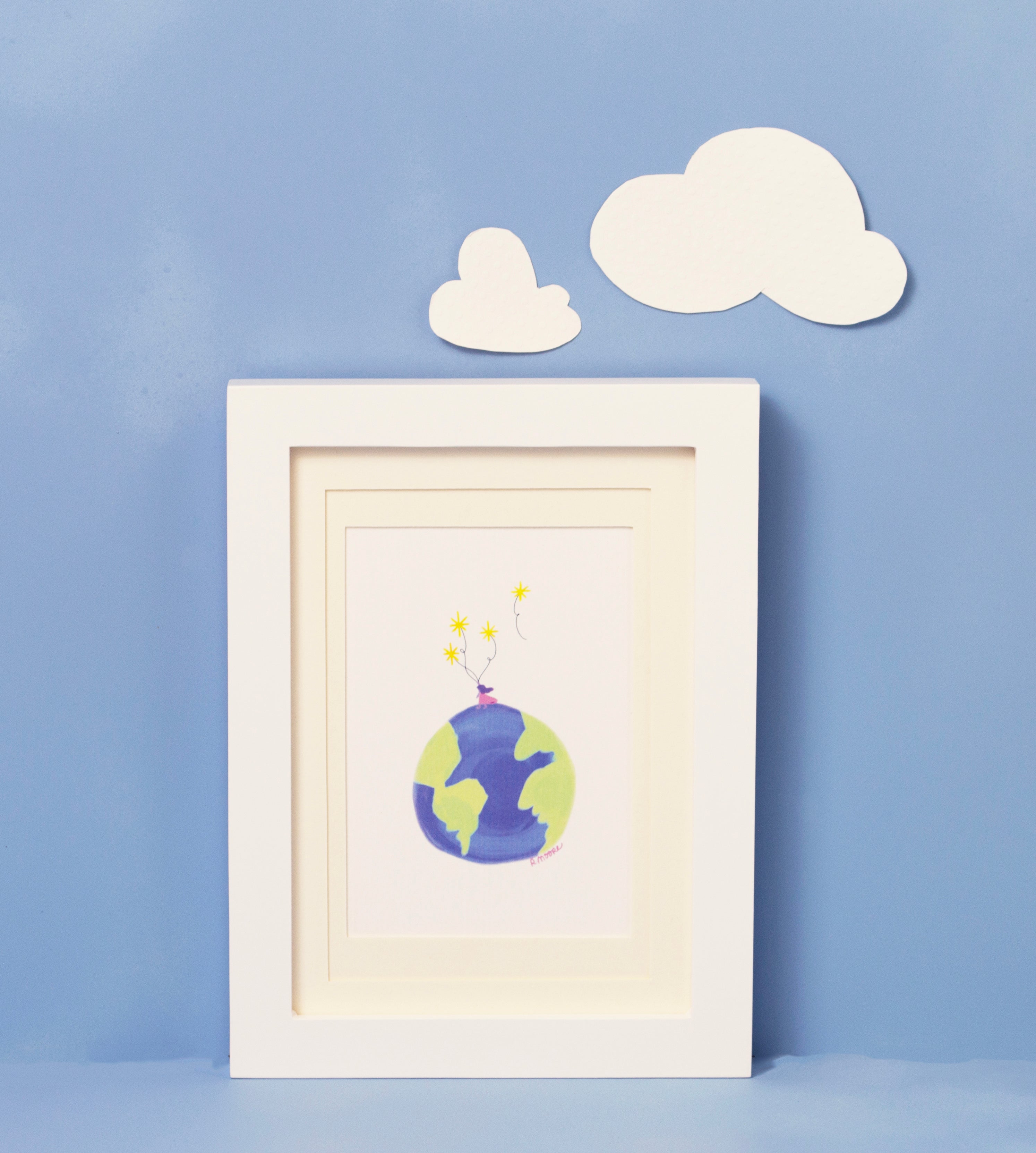 Girl on Top of the World framed print of a hand illustrated Girl in a pink dress standing on top of the world holding stars as balloons against  white background. The framed print is shot against a blue background with two white clouds above the framed print. The frame is white, and the matting is ivory
