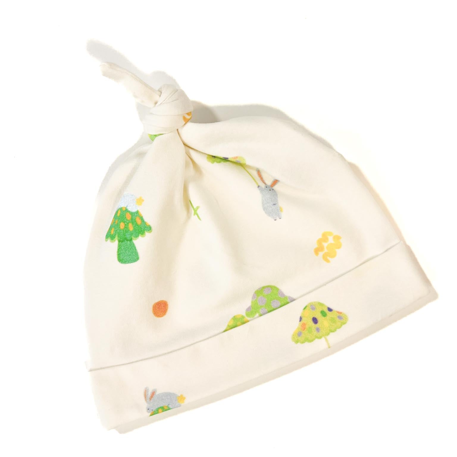 An ivory organic cotton baby beanie hat featuring a pattern of playful bunnies and toadstools in the forest. 