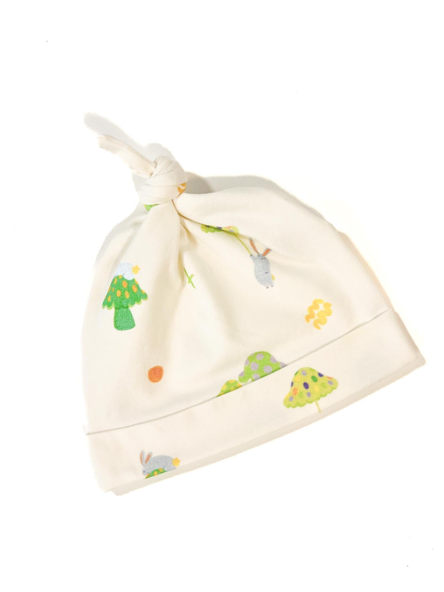 An ivory organic cotton baby beanie hat featuring a pattern of playful bunnies and toadstools in the forest. 
